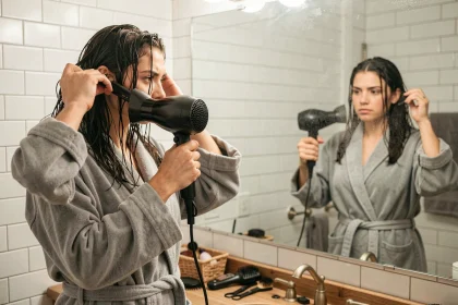 Jeune femme débutante utilisant une brosse soufflante devant un miroir de salle de bain